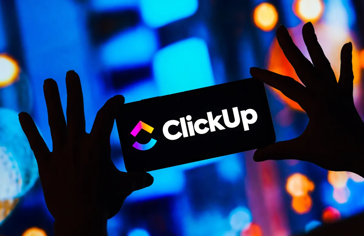 Letreiro luminoso com a marca ClickUp e mãos em primeiro plano